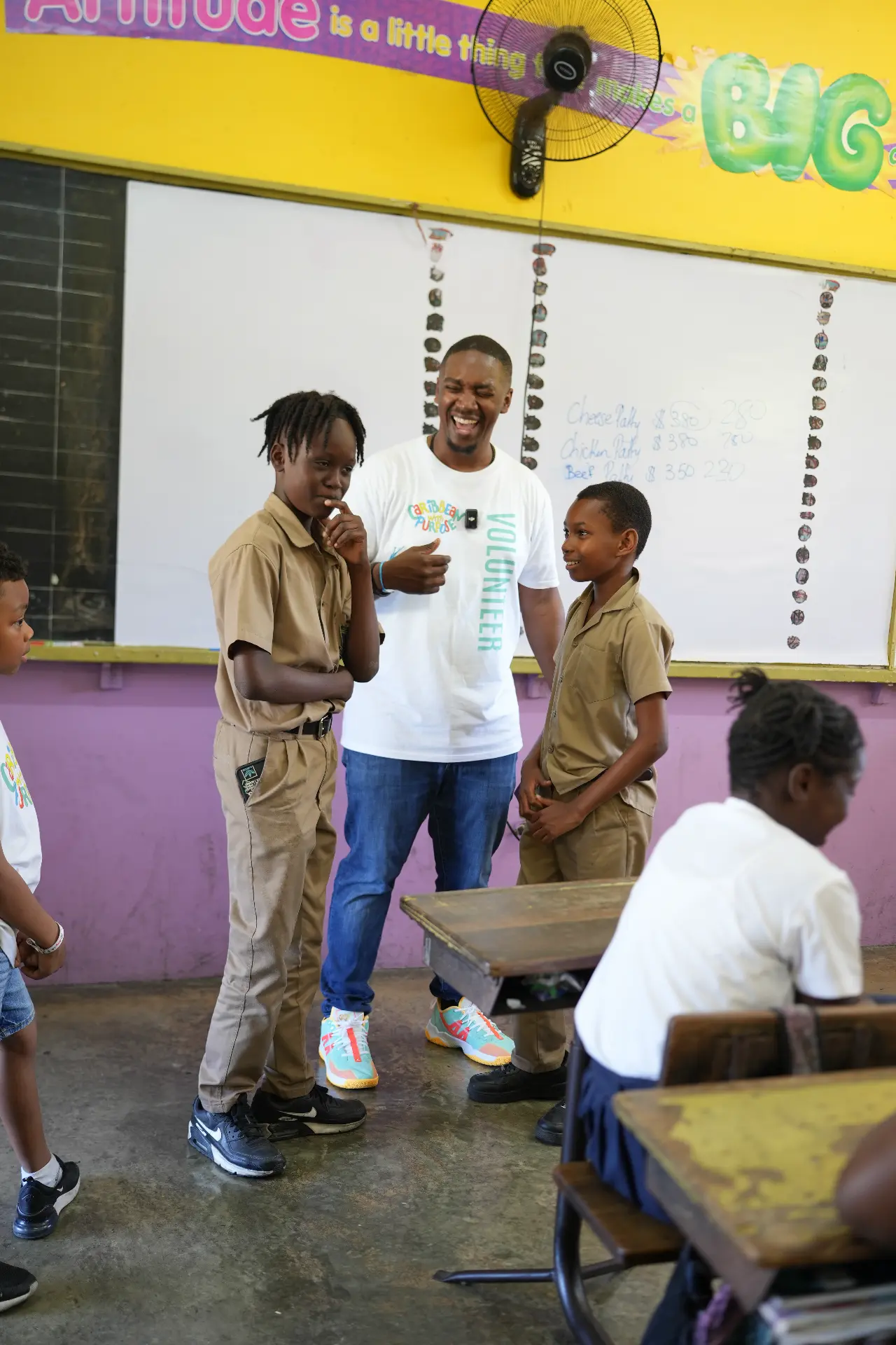 A Caribbean With Purpose volunteer talking and laughing with two students in their classroom