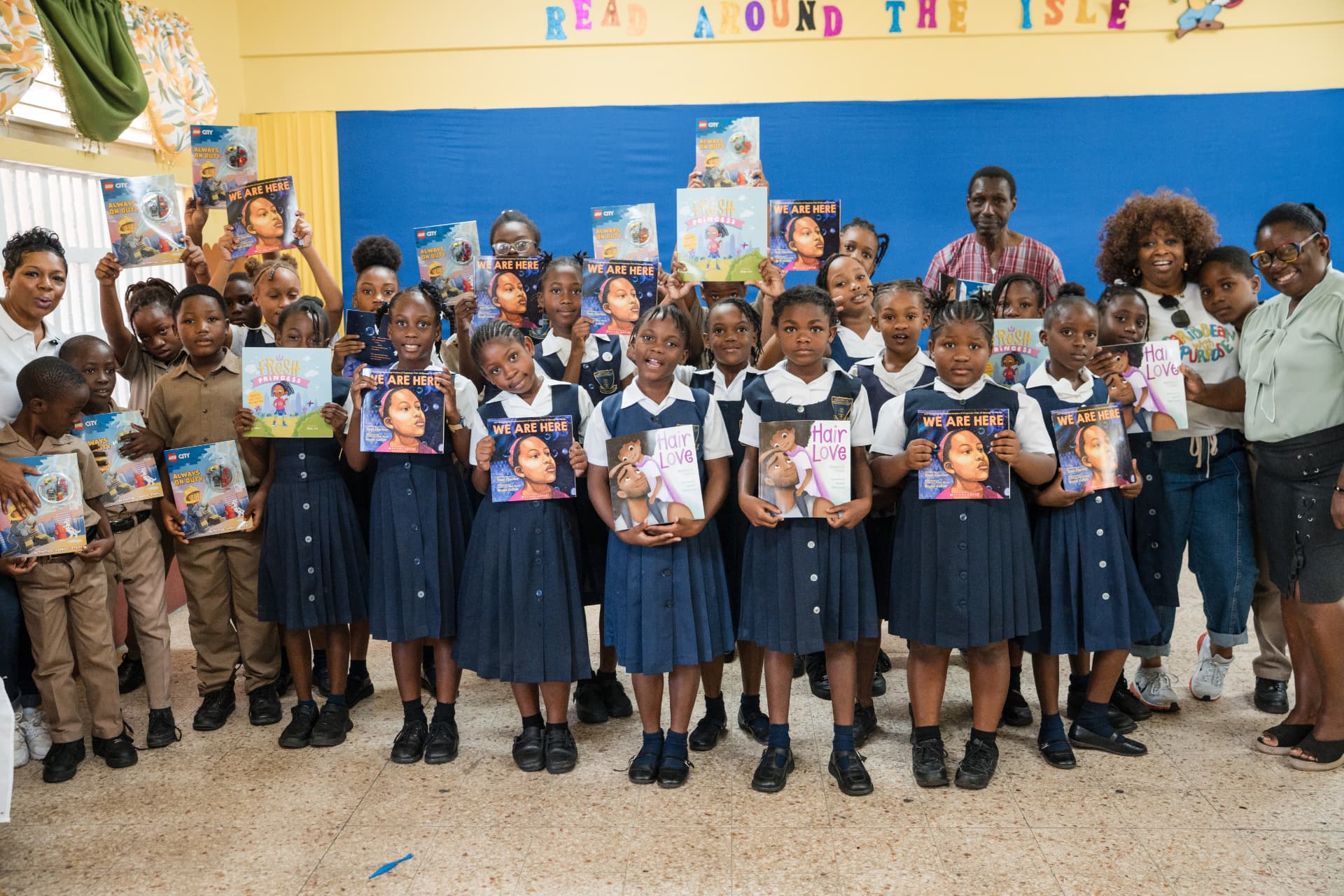 A class of primary-grade students holding new books with their educators